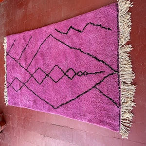 May include: A pink and black Moroccan rug with a geometric pattern. The rug has a fringe border.