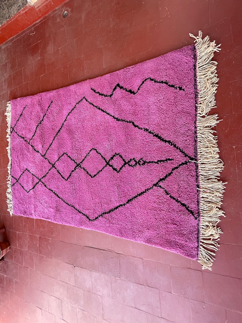 May include: A pink and black Moroccan rug with a geometric pattern. The rug has a fringe border.