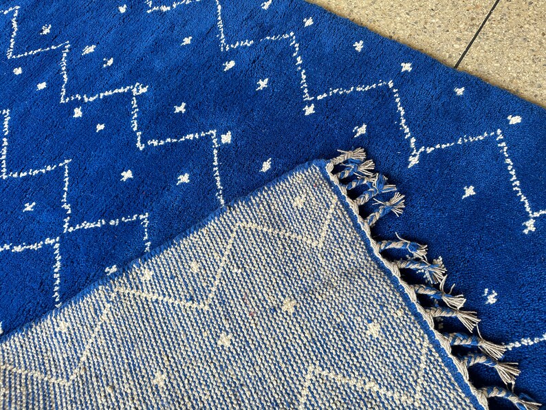 Puede incluir: Dos alfombras azules y blancas con flecos. La alfombra de arriba tiene un patr&oacute;n geom&eacute;trico y la alfombra de abajo tiene un patr&oacute;n m&aacute;s intrincado.