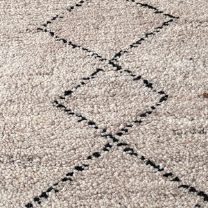 May include: A close-up of a beige rug with a black diamond pattern. The rug is made of a soft, fluffy material.