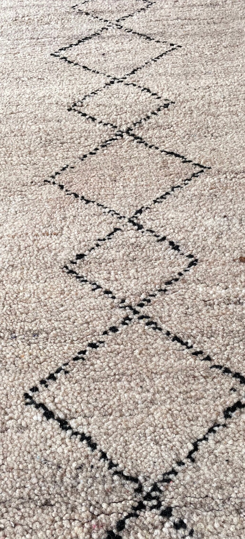 May include: A close-up of a beige rug with a black diamond pattern. The rug is made of a soft, fluffy material.