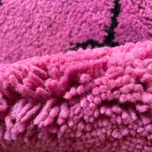 May include: Close-up of a pink and black rug with a fuzzy texture. The rug is made of soft, fluffy fibers.