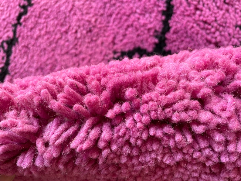May include: Close-up of a pink and black rug with a fuzzy texture. The rug is made of soft, fluffy fibers.
