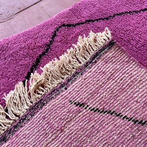 May include: Two pink and cream woven rugs with black geometric designs and fringe edges. The rugs are layered on top of each other.