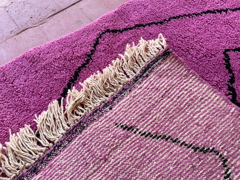 May include: Two pink and cream woven rugs with black geometric designs and fringe edges. The rugs are layered on top of each other.