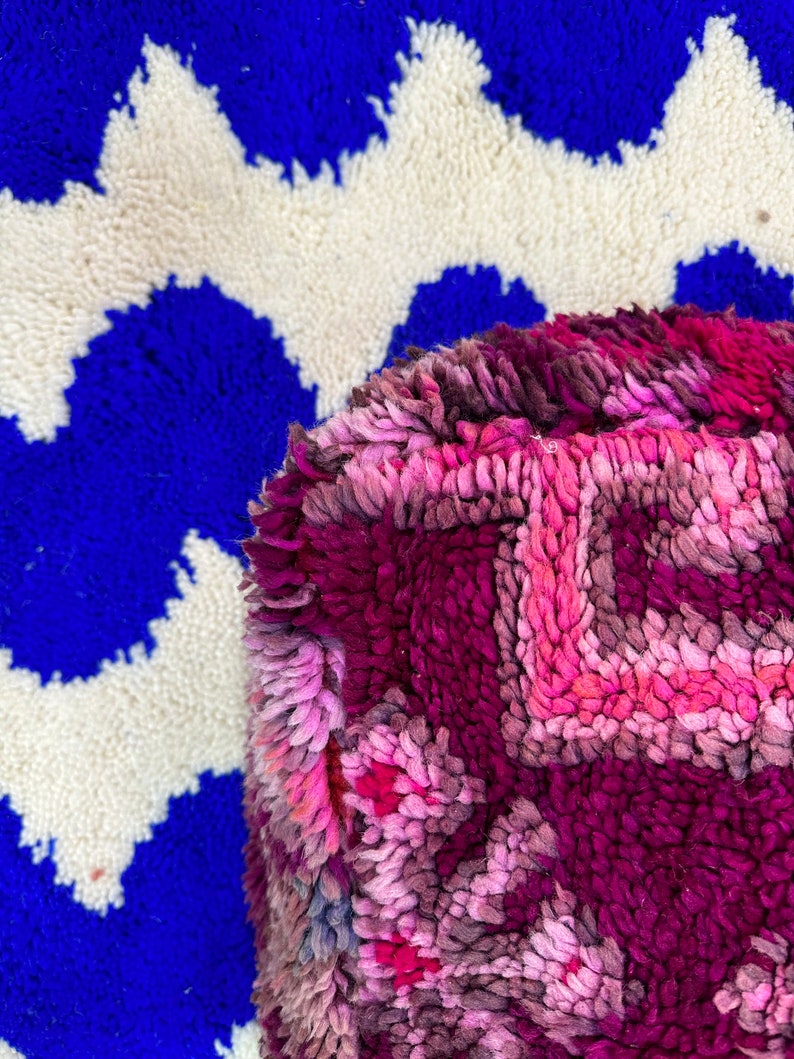 Pu&ograve; includere: Primo piano di un tappeto vibrante e strutturato con un motivo geometrico. Il tappeto presenta uno sfondo blu intenso con forme a zig-zag bianche. Una sezione di un tappeto rosa e viola con un disegno floreale &egrave; in primo piano.
