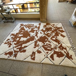 May include: A white and brown patterned rug with a geometric design. The rug has a fringe border.
