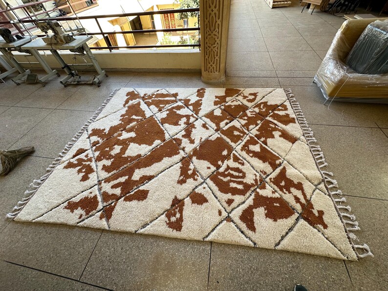 May include: A white and brown patterned rug with a geometric design. The rug has a fringe border.