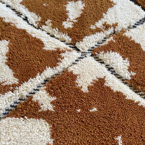 May include: A close-up of a brown and white patterned rug with a geometric design. The rug is made of a soft, fluffy material.