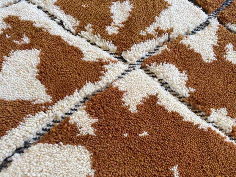 May include: A close-up of a brown and white patterned rug with a geometric design. The rug is made of a soft, fluffy material.
