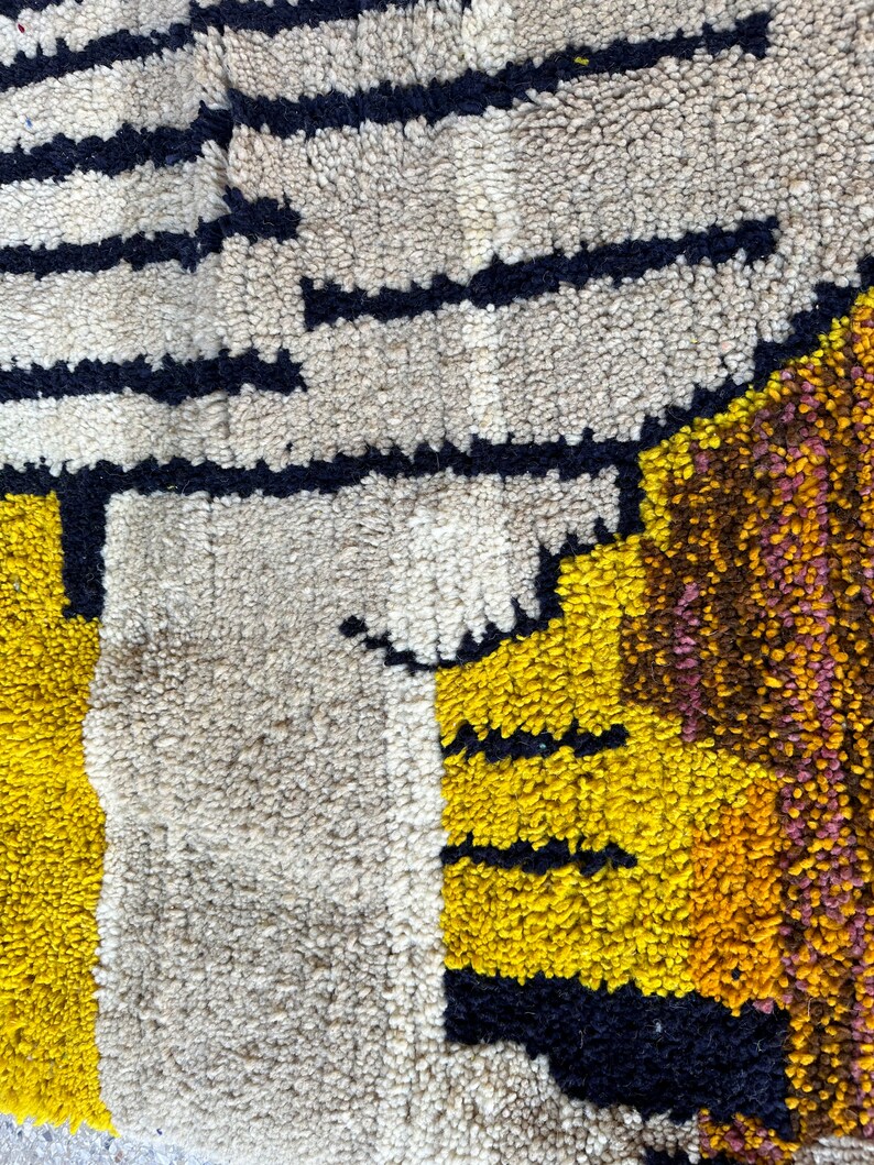 Puede incluir: Primer plano de una alfombra abstracta colorida con formas geom&eacute;tricas en tonos de amarillo, marr&oacute;n, negro y blanco. La alfombra est&aacute; hecha de un material grueso y texturizado.