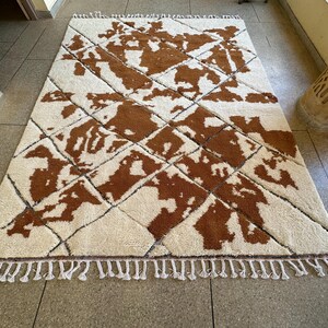 May include: A white and brown patterned rug with a diamond pattern. The rug has a fringe border.