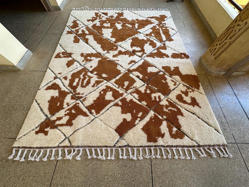 May include: A white and brown patterned rug with a diamond pattern. The rug has a fringe border.