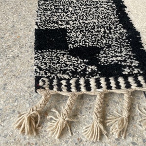 May include: Black and white rug with a geometric pattern and fringe. The rug has a black and white chevron border.