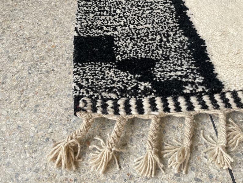 May include: Black and white rug with a geometric pattern and fringe. The rug has a black and white chevron border.