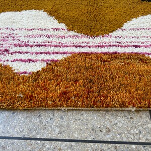 May include: Close-up of a brown, orange, white, and pink shag rug with a geometric pattern. The rug has a thick pile and is made of soft, plush fibers.