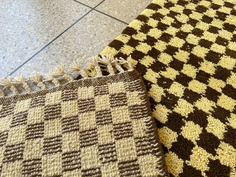 May include: Two woven rugs with a checkered pattern in brown and cream. The rug on the left has a fringe border.