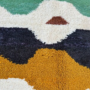 May include: A close-up of a colorful rug with abstract shapes in shades of green, white, black, brown, and yellow. The rug has a soft, fluffy texture.
