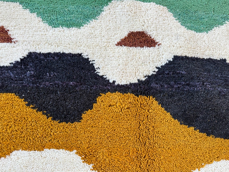 May include: A close-up of a colorful rug with abstract shapes in shades of green, white, black, brown, and yellow. The rug has a soft, fluffy texture.