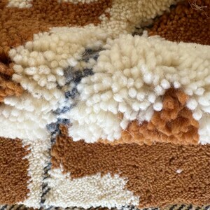 May include: Close-up of a brown, white, and blue woven rug with a textured, fluffy surface.