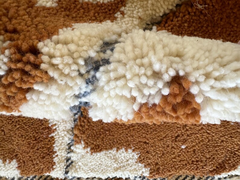 May include: Close-up of a brown, white, and blue woven rug with a textured, fluffy surface.