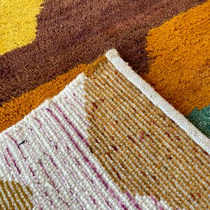 May include: Close-up of a multi-colored woven rug with a brown, yellow, and white pattern. The rug has a textured surface and a white border.