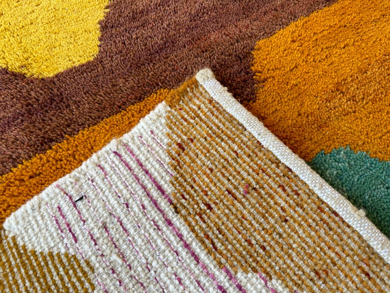 May include: Close-up of a multi-colored woven rug with a brown, yellow, and white pattern. The rug has a textured surface and a white border.
