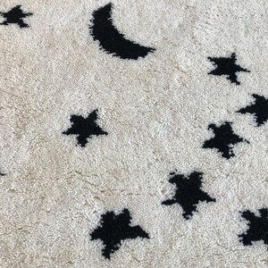 May include: A white rug with a black crescent moon and stars design. The rug is made of a soft, fluffy material.