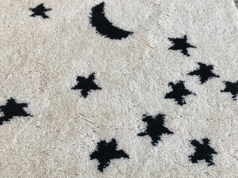 May include: A white rug with a black crescent moon and stars design. The rug is made of a soft, fluffy material.