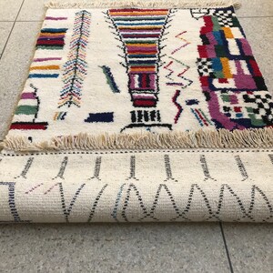 May include: A white rug with a colorful geometric pattern. The rug has a fringe border and is rolled up.