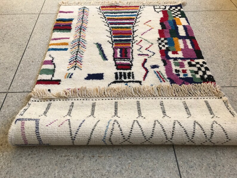 May include: A white rug with a colorful geometric pattern. The rug has a fringe border and is rolled up.