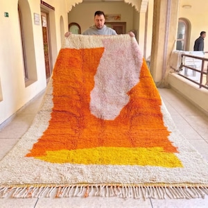 Handmade Moroccan rug in warm orange tones with abstract geometric pattern placed in a cozy modern living room
