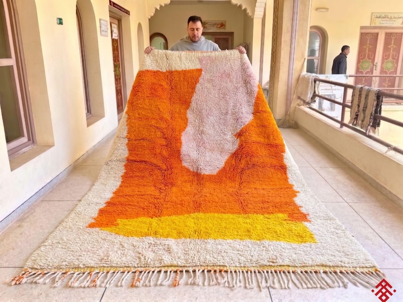 Handmade Moroccan rug in warm orange tones with abstract geometric pattern placed in a cozy modern living room