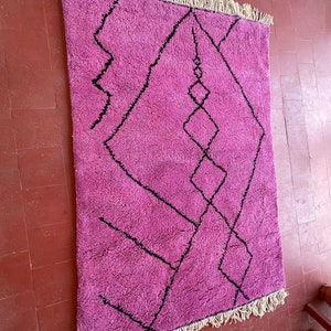 May include: A pink and black Moroccan rug with a geometric pattern. The rug has a fringe border.