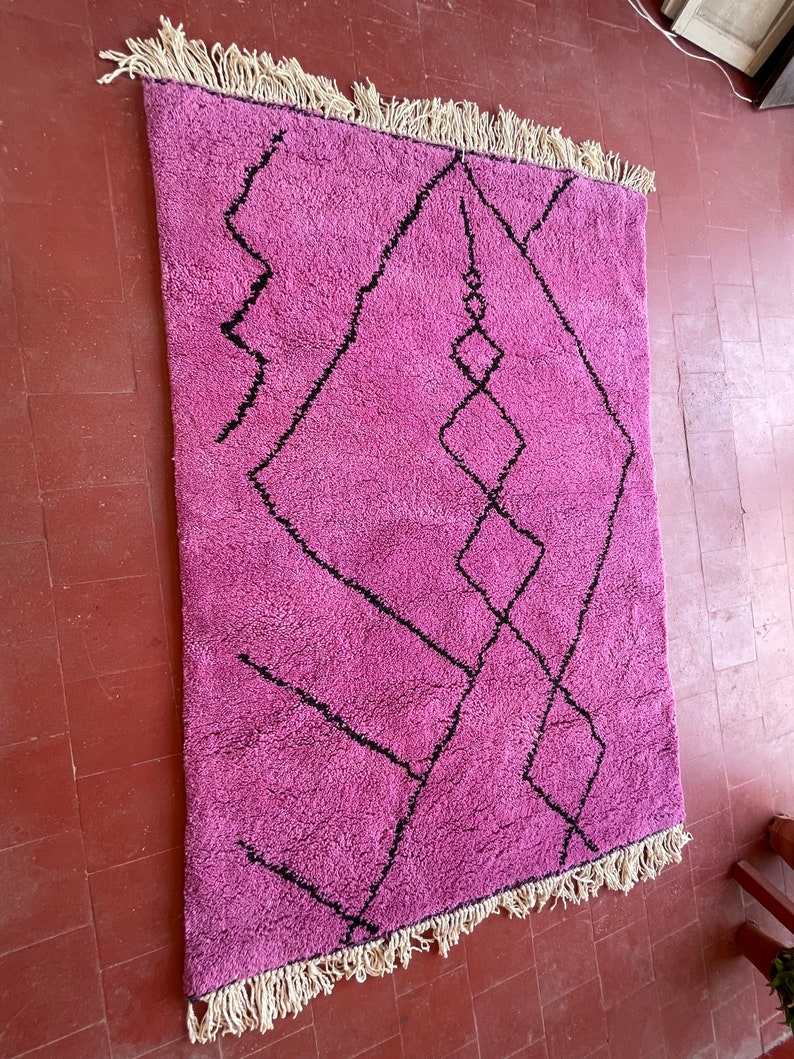 May include: A pink and black Moroccan rug with a geometric pattern. The rug has a fringe border.