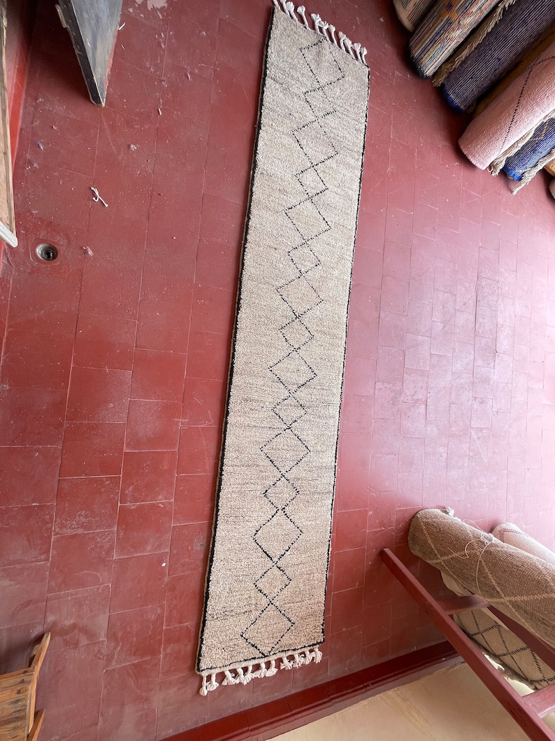 May include: A long, off-white runner rug with a black diamond pattern. The rug has fringe on the ends.