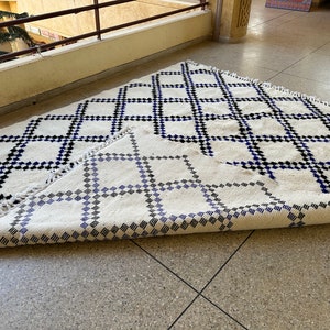 May include: A white rug with a black and blue geometric pattern. The rug is folded in half, revealing the pattern on both sides.