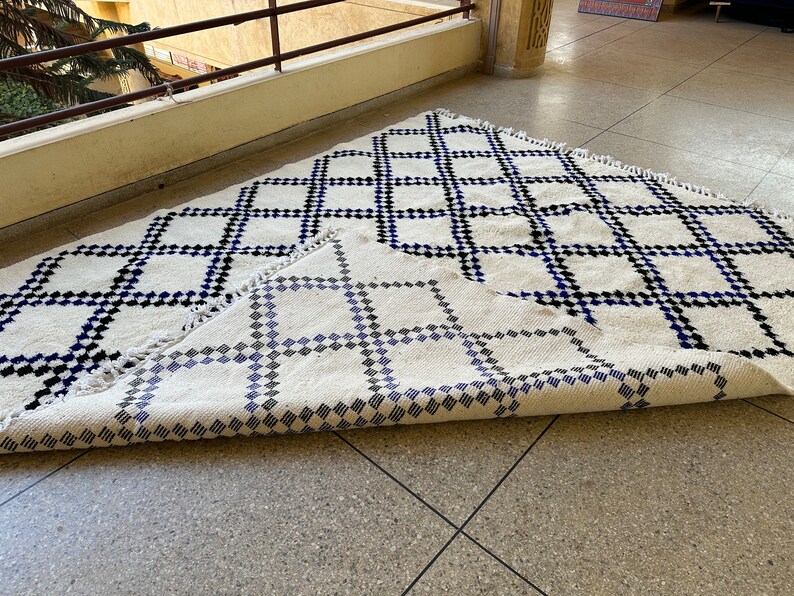 May include: A white rug with a black and blue geometric pattern. The rug is folded in half, revealing the pattern on both sides.