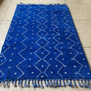 Puede incluir: Una alfombra marroqu&iacute; azul y blanca con un patr&oacute;n de diamantes y flecos.