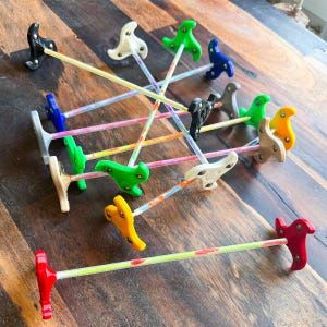 Könnte beinhalten: Eine Sammlung farbenfroher, abstrakt geformter Objekte mit einem T-förmigen Griff und einem langen, dünnen, geraden Stiel. Die Objekte sind in verschiedenen Farben gehalten, darunter Rot, Gelb, Grün, Blau, Schwarz, Weiß und Grau. Die Stiele haben ein Regenbogenmuster.