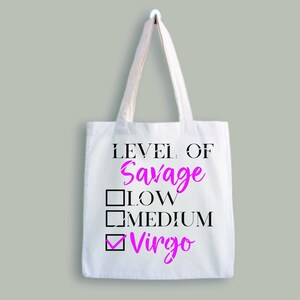May include: White tote bag with the text "LEVEL OF SAVAGE" in black. A checklist with the options "LOW", "MEDIUM", and "Virgo" is below the text. The word "Virgo" is checked and written in pink.