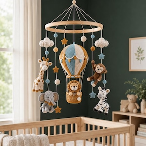 May include: A hanging nursery mobile featuring a central crocheted hot air balloon with a lion in the basket. Surrounding the balloon are crocheted figures of a giraffe, elephant, monkey, and zebra, accented with small clouds, stars, and spheres.