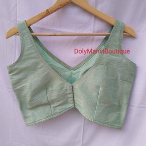 May include: A light green sleeveless blouse with a V-neckline. The blouse is made of a soft, silky fabric and has a simple, elegant design. The text "DolyManviBoutique" is visible on the blouse.