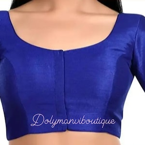 Könnte beinhalten: Eine königlich blaue Bluse mit kurzen Ärmeln, einem runden Ausschnitt und einem Knopfverschluss vorne. Die Bluse ist aus einem glatten, seidenartigen Stoff gefertigt. Der Text "Dolymanviboutique" ist auf der Vorderseite der Bluse aufgedruckt.