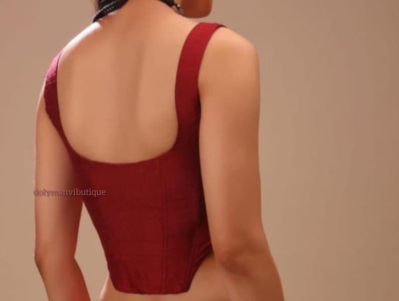 May include: A maroon sleeveless top with a square neckline and a fitted bodice. The top is made of a textured fabric and has a slightly pointed hem.