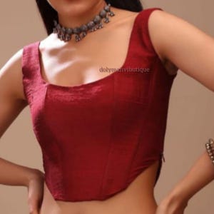 May include: A maroon sleeveless top with a square neckline and a fitted bodice. The top is cropped and has a slightly asymmetrical hemline.