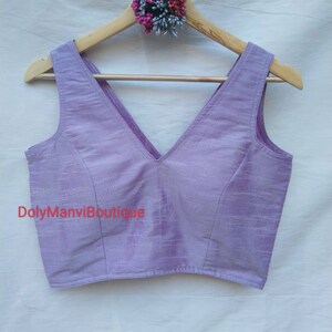 May include: A lavender sleeveless blouse with a deep V-neckline. The blouse is made of a soft, silky fabric and has a subtle sheen. The text "DolyManviBoutique" is printed on the front of the blouse.