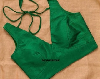 Puede incluir: Una blusa verde sin mangas con un escote en V profundo y un cierre de lazo en la espalda. La blusa tiene un corpiño ajustado y un ajuste holgado.