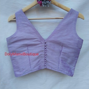 May include: A lavender sleeveless blouse with a deep V-neckline and button closure. The blouse is made of a soft, silky fabric and has a cropped fit.