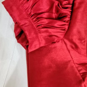 May include: A red satin fabric with a gathered, puffed sleeve detail. The fabric is smooth and shiny.